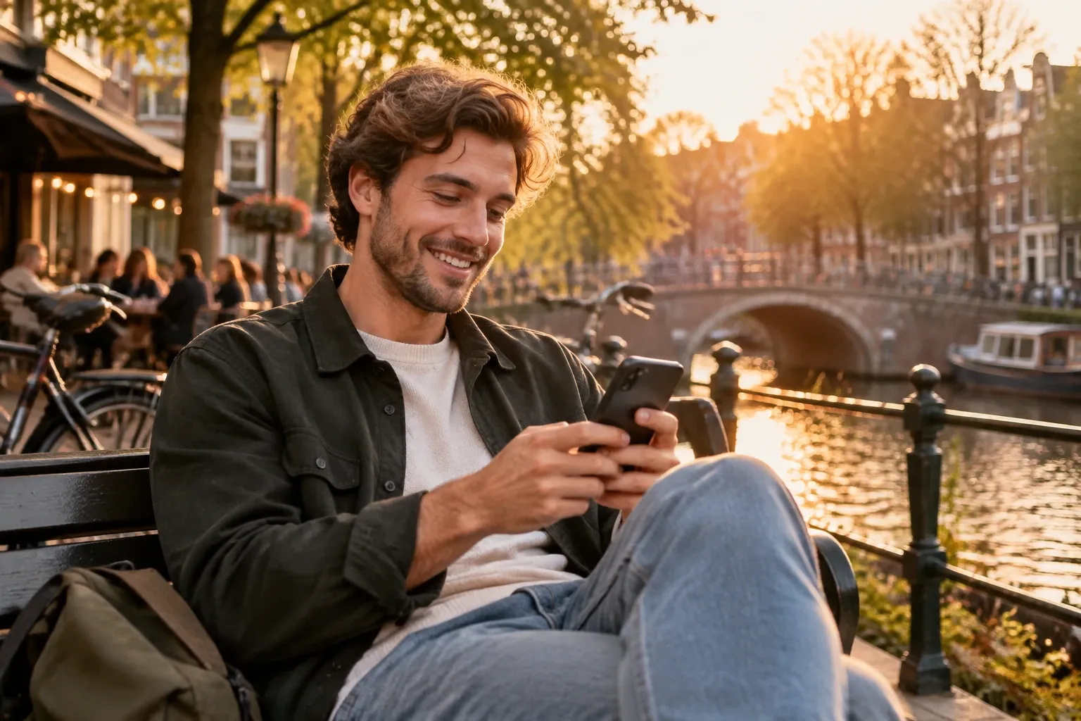 Man op bankje langs gracht kijkt lachend naar smartphone bij ondergaande zon